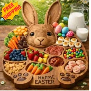 May include: A wooden Easter bunny-shaped serving platter filled with various snacks, including fruits, cheeses, and meats. The platter has a carved bunny face and ears, with the words "HAPPY EASTER" at the bottom. A pitcher of milk and a glass of milk are in the background.