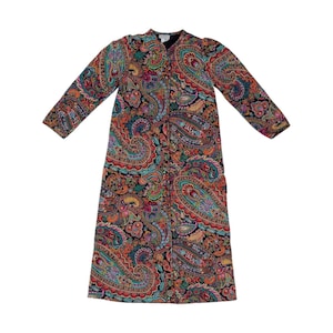 May include: A long-sleeved robe featuring a vibrant, multi-colored paisley pattern on a black background. The garment has a straight silhouette, a round neckline, and a full-length front opening with visible buttons, showcasing intricate floral motifs.