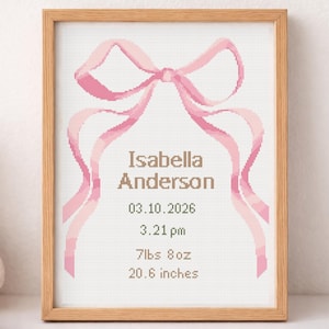 May include: A framed cross-stitch birth announcement with a pink bow design. The text reads "Isabella Anderson" with the birth date, time, weight (7lbs 8oz), and length (20.6 inches). The frame is made of light wood.