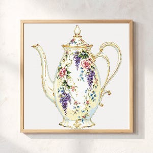 May include: A square framed cross-stitch pattern featuring a cream-colored teapot decorated with intricate floral motifs, including pink roses and purple wisteria clusters. The teapot has a gold-trimmed handle, spout, and lid with a finial.
