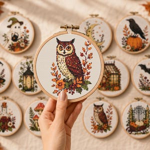 Può includere: Una collezione di telai da ricamo circolari in legno con disegni a punto croce a tema autunnale e di Halloween, tra cui un gufo, un fantasma, un corvo su una zucca, un cappello da strega, una lanterna, una serra, un pipistrello e funghi.