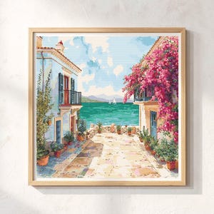 Könnte beinhalten: Ein gerahmtes Aquarellgemälde zeigt eine Küstenlandschaft. Zwei Gebäude mit Balkonen flankieren einen Steinweg, der zum türkisfarbenen Meer führt. Rosa Bougainvillea fällt von den Balkonen. Topfpflanzen säumen den Weg.