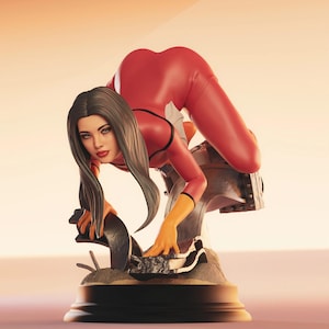 May include: A red bodysuit with black accents is worn by a figure in a dynamic pose. The figure has long dark hair and orange gloves. The statue is mounted on a detailed base with a metallic structure, set against a warm, gradient background.