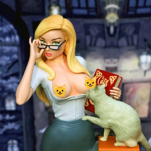 May include: A blonde figurine wearing black-rimmed glasses, a white short-sleeved top, and a dark skirt. The figure holds a red book with the word Cats printed in gold. A light-colored cat stands on an orange base next to the figure.