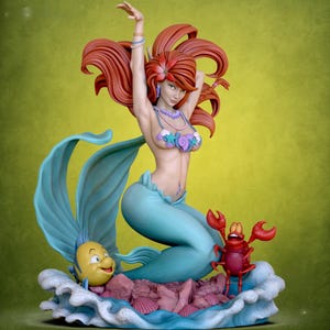 May include: A detailed figurine of a mermaid with flowing red hair, a seashell top, and a turquoise tail. The mermaid is posed with her arms raised. A yellow fish and a red crab are also featured in the scene, set on a wave-like base.