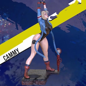 Puede incluir: Figura de un personaje femenino en una pose dinámica, con una chaqueta azul, un body negro y botas rojas. La figura tiene el pelo rubio y está de pie sobre una plataforma. La palabra "CAMMY" está impresa en la base.