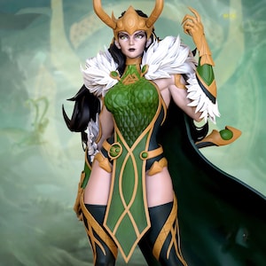 Puede incluir: Figura detallada de un personaje con un disfraz verde y dorado con capa. La figura tiene pelo largo negro, una corona dorada y detalles de plumas blancas. La pose es dinámica, con un brazo levantado.