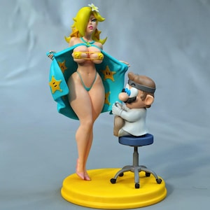 May include: A figurine featuring a blonde character with a white flower in her hair, wearing a teal cape with yellow star patterns, and a smaller character dressed in a white medical coat and head mirror, sitting on a blue stool on a yellow base.