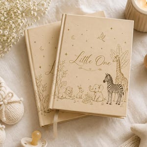 May include: Two beige hardback books with the text Little One and illustrations of a lion, rabbit, elephant, zebra, and giraffe. The covers feature stars and moon accents. The books are surrounded by baby booties, a rattle, and a candle.