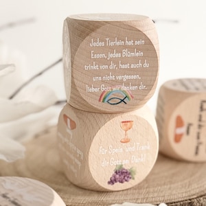 Könnte beinhalten: Holzwürfel mit religiösen Inschriften und Illustrationen. Ein Würfel zeigt einen Regenbogen, einen Fisch und Text. Ein anderer Würfel hat einen Kelch, Trauben und Text. Die Würfel sind hellbraun und scheinen handgefertigt zu sein.