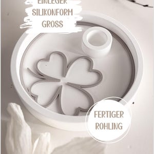 Könnte beinhalten: Eine weiße Silikonform mit einem grauen vierblättrigen Kleeblatt-Design im Inneren. Die Form ist rund und enthält ein kleines, zylindrisches Teil. Der Text auf dem Bild lautet "EINLEGER SILIKONFORM GROSS" und "FERTIGER ROHLING".