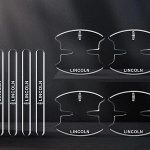 Könnte beinhalten: Ein Set aus vier transparenten, rechteckigen Türkantenschonern und vier transparenten, geschwungenen Türgriffschalen-Schutzfolien, jeweils mit dem weißen Schriftzug und Logo von Lincoln versehen. Diese Autozubehörteile dienen dem Schutz.