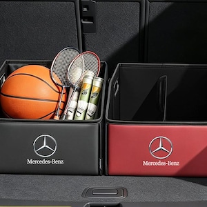 May include: Two rectangular storage organizers with the Mercedes-Benz logo. The left box is black and contains an orange basketball, two badminton rackets, and two shuttlecock tubes. The right box is red and features an internal divider.