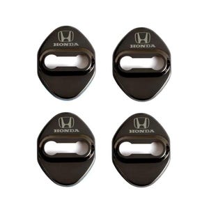 May include: A set of four black metallic car door lock covers, each featuring a smooth, rounded diamond shape with a central horizontal cutout. The Honda logo and the word HONDA are engraved in a light silver tone at the top of each piece.