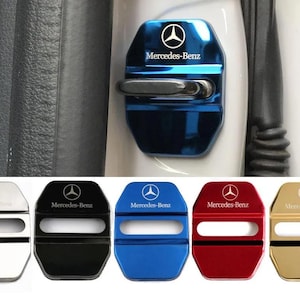 May include: A set of five metallic car door lock covers in silver, black, blue, red, and gold. Each cover features the Mercedes-Benz logo and text, with a horizontal cutout. One blue cover is shown installed on a white car door latch.