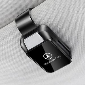 Peut inclure: Un clip porte-lunettes de soleil pour pare-soleil de voiture noir, doté d'un panneau avant rectangulaire brillant avec le logo et le texte Mercedes-Benz imprimés en blanc au centre. L'accessoire présente une structure en plastique robuste.