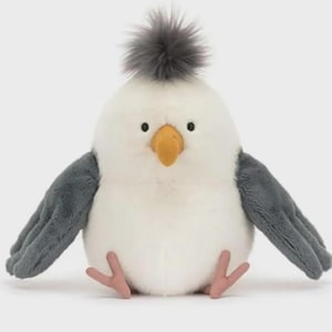 May include: A plush white bird with gray wings and a gray tuft on its head. The bird has a yellow beak and small black eyes. Its feet are pink. This soft toy is designed for children.