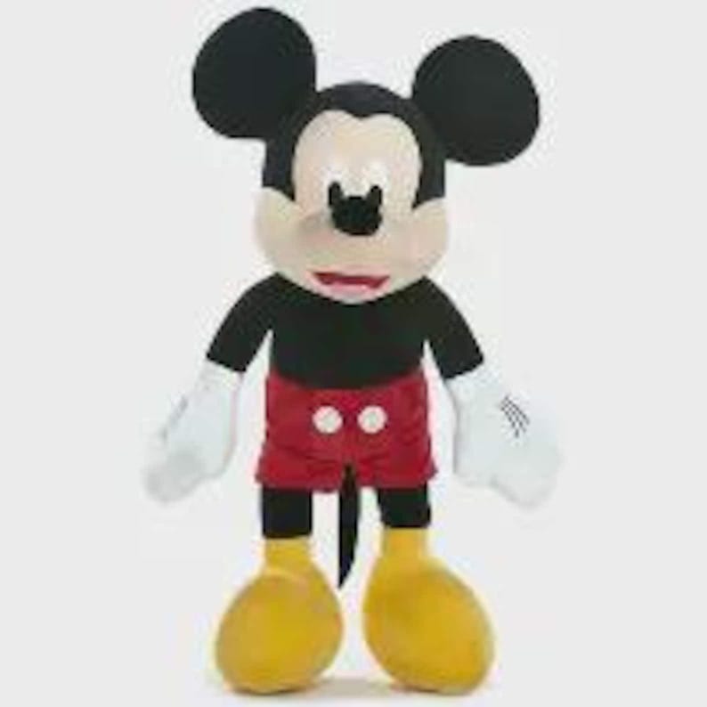 May include: A plush Mickey Mouse toy, with a black body, red shorts, and yellow shoes. The character has large black ears, a tan face, and white gloves. The toy is standing upright against a white background.
