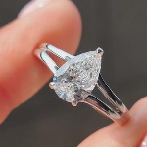 Peut inclure: Une bague en diamant en forme de poire avec une monture fendue. La bague présente un grand diamant clair serti dans un anneau en argent. L'anneau se divise en deux lignes parallèles à l'approche du diamant, créant un look moderne et élégant.