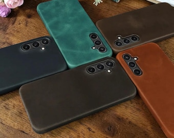 Puede incluir: Cinco fundas para smartphone en varios colores, incluyendo verde, marrón oscuro, negro y tostado. Cada funda presenta un acabado mate liso y una sección recortada para un sistema de cámara de triple lente con flash integrado, alineados verticalmente.