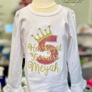 Peut inclure: Chemise blanche &agrave; manches longues avec une couronne dor&eacute;e et un chiffre 5 rose brod&eacute;s sur le devant. Le texte "Her Royal Fiveness Meyah" est &eacute;galement brod&eacute; en or.