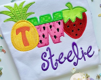 Puede incluir: Una camiseta blanca con un diseño bordado de colores de una piña, una sandía y una fresa que deletrean "DOS". El nombre "Steelye" está bordado en morado debajo del diseño de la fruta.