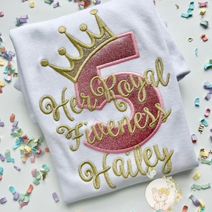 Peut inclure: T-shirt blanc avec broderie dor&eacute;e qui dit "Her Royal Highness Hailey" avec un chiffre 5 en paillettes roses et une couronne en paillettes dor&eacute;es.