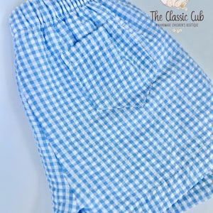 Puede incluir: Shorts de cuadros vichy azul claro y blanco con cintura el&aacute;stica y un bolsillo trasero. Los shorts est&aacute;n hechos de una tela ligera. The Classic Cub, una boutique infantil hecha a mano, est&aacute; impresa en la parte superior derecha.