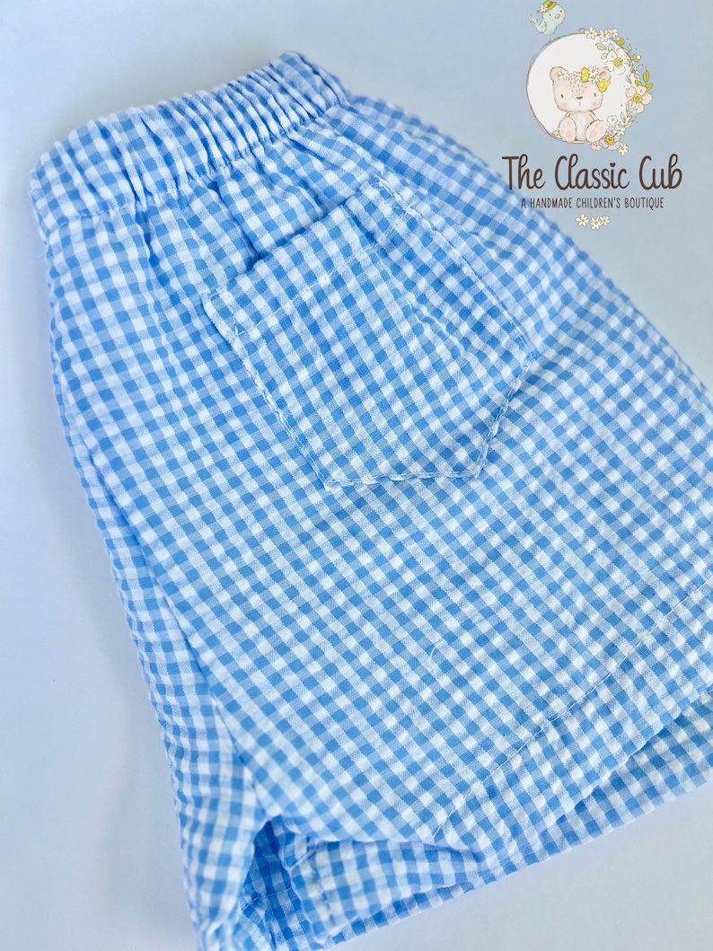 Puede incluir: Shorts de cuadros vichy azul claro y blanco con cintura el&aacute;stica y un bolsillo trasero. Los shorts est&aacute;n hechos de una tela ligera. The Classic Cub, una boutique infantil hecha a mano, est&aacute; impresa en la parte superior derecha.