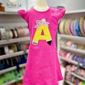 Vestido escolar rosa para niñas con diseño de lápiz.
