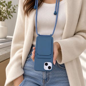 Può includere: Una custodia per smartphone blu opaco con uno scomparto portacarte integrato sul retro, fissata a un cordino blu abbinato con cursori regolabili, progettata per essere indossata al collo per trasportare il dispositivo mobile a mani libere.