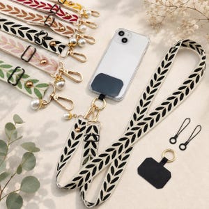 Puede incluir: Una colección de correas ajustables para teléfono con un patrón de hojas repetitivo en varios colores, incluyendo rojo, negro, rosa y verde. Cada correa incluye herrajes dorados, un detalle de perla y un conector adhesivo negro para teléfono.