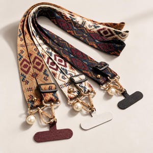 Peut inclure: Trois bandoulières réglables avec des motifs géométriques tissés en beige, blanc et gris foncé. Chaque sangle comprend des ferrures métalliques dorées, un curseur en plastique noir, une perle blanche et une attache en tissu en forme de T.