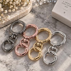Può includere: Quattro chiusure girevoli circolari in metallo disposte in fila, con finiture canna di fucile, oro rosa, oro e argento. Ogni chiusura è composta da un grande anello a molla collegato a un anello circolare più piccolo tramite un perno.