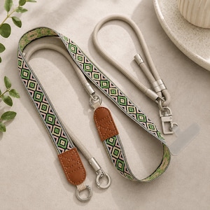 Könnte beinhalten: Ein Handy-Lanyard mit einem gewebten Band in einem geometrischen Rautenmuster in Grün, Pink und Schwarz. Das Band verfügt über braune Kunstlederakzente, silberfarbene Metall-Drehverschlüsse und eine transparente Kunststofflasche zur Befestigung.