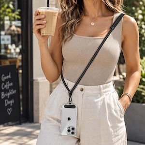 May include: A clear smartphone case with a black top accent attached to a long, thin black crossbody strap. The case features a visible Apple logo on the back of the phone and is designed to be worn around the torso for hands-free carrying convenience.
