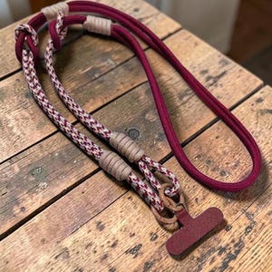 Op de afbeelding: Een hondenriem met een effen bordeauxrood touwgedeelte en een gedeelte met een bordeauxrood en wit pied-de-poulepatroon. De riem is voorzien van beige koordwikkelingen op de verbindingspunten en een T-vormige bordeauxrode handgreep.