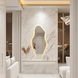 May include: An interior design featuring a modern, abstract-shaped mirror with a warm, glowing outline. The mirror is mounted on a marble-patterned wall, above a white console table. The room has a minimalist aesthetic with white furniture and decor.