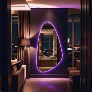 May include: An irregular, organic-shaped wall mirror featuring a vibrant purple LED backlight. The mirror is mounted on a dark wall and reflects a marble-topped console table with various glass bottles and a dark interior room setting.