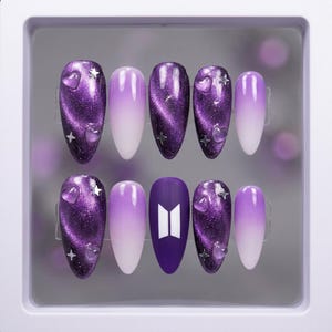 May include: A set of ten purple and white ombre press-on nails. Some nails feature a glittery cat-eye effect, clear heart and star accents. One nail has the BTS logo in white.