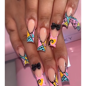 May include: Long, square-shaped acrylic nails with a light pink base and a French tip. The nails feature a Sally-inspired design with black stitching, and colorful accents of yellow, blue, and pink. Some nails have small black bow accents.