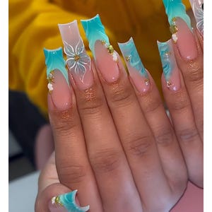 Puede incluir: Uñas acrílicas largas y cuadradas con un diseño degradado. Las uñas hacen la transición de una base rosa claro a un patrón de remolino turquesa y blanco. Algunas uñas presentan diseños florales blancos y detalles dorados.