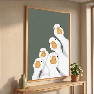 May include: A framed art print depicting five white geese with orange beaks, peering out with curiosity. The geese are set against a muted green backdrop, creating a playful aesthetic. The artwork is framed in a light wood, adding a touch of natural warmth.