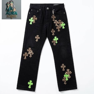 Può includere: Jeans in denim nero con chiusura a bottoni e un ciondolo in metallo argentato attaccato al passante della cintura. I pantaloni sono decorati con molteplici toppe a forma di croce con motivo leopardato marrone e colore verde neon.
