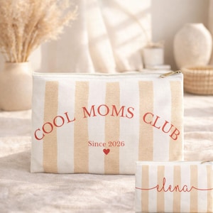 May include: Cream and white striped zippered pouch with "COOL MOMS CLUB" in red lettering, a small red heart, and "Since 2026". A smaller pouch with "elena" in red script is also visible.