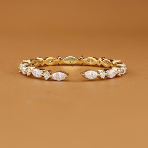 May include: A gold open-style ring featuring a series of marquise-cut and round-cut clear stones arranged in a continuous pattern along the band. The ring displays a small letter A logo in the center and the text AVIRA FINE JEWELRY at the bottom.