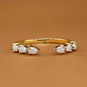 May include: A gold open-style ring featuring six pear-cut white stones arranged in two groups of three on either side of the band. The ring has a polished yellow gold finish and includes the text AVIRA FINE JEWELRY in the bottom right corner.