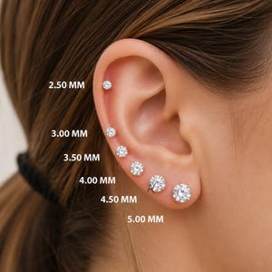 May include: A close-up of an ear with six diamond stud earrings of varying sizes, ranging from 2.50 mm to 5.00 mm. The earrings are set in a classic style, showcasing their brilliance. The text "AVIRA FINE JEWELRY" is visible.