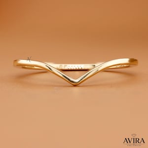 May include: A polished gold V-shaped chevron ring with a smooth, reflective surface. The band features a distinct pointed center design. The text AVIRA FINE JEWELRY with a small diamond icon is visible in the bottom right corner of the image.