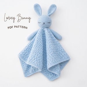 Könnte beinhalten: Ein hellblauer Häkel-Schmusetier-Hase mit langen Ohren und einem kleinen deckenartigen Körper. Das Gesicht hat gestickte geschlossene Augen und eine einfache Kreuzstich-Nase. Der Text "Lovey Bunny PDF PATTERN" steht oben links in Schwarz.